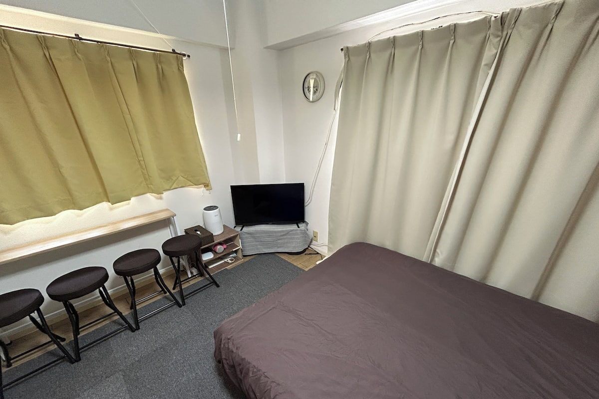 Un dormitorio con cama, televisor, escritorio con silla y ventana con cortinas.