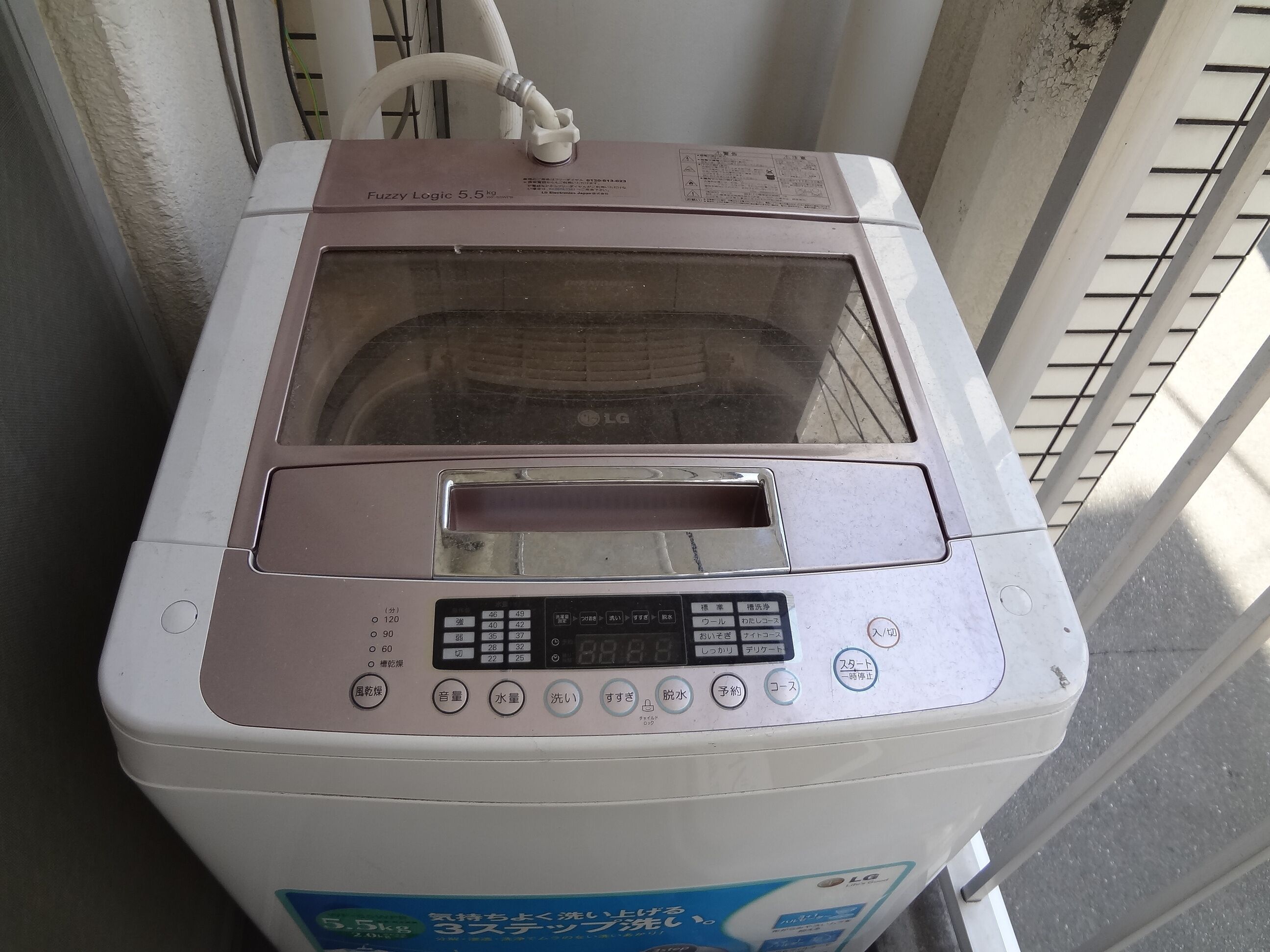Máquina de lavar roupa com painel de comandos, mangueira de entrada de água e etiqueta a indicar que é um modelo de 5,5kg.