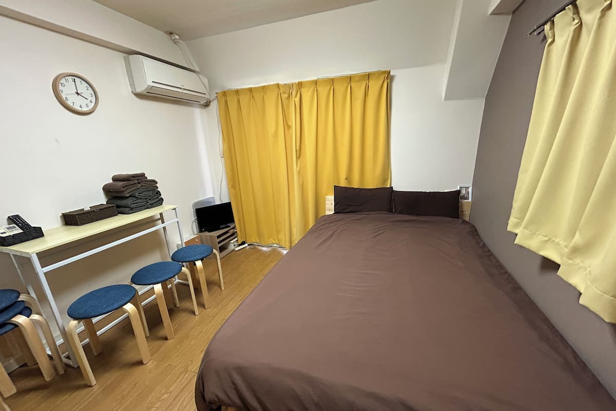 Un dormitorio con cama, un escritorio con sillas, televisor y aire acondicionado.