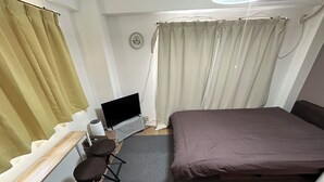 Ein Schlafzimmer mit einem Bett, einem Schreibtisch mit Computer, einem Sessel und einem Fenster mit Vorhängen.