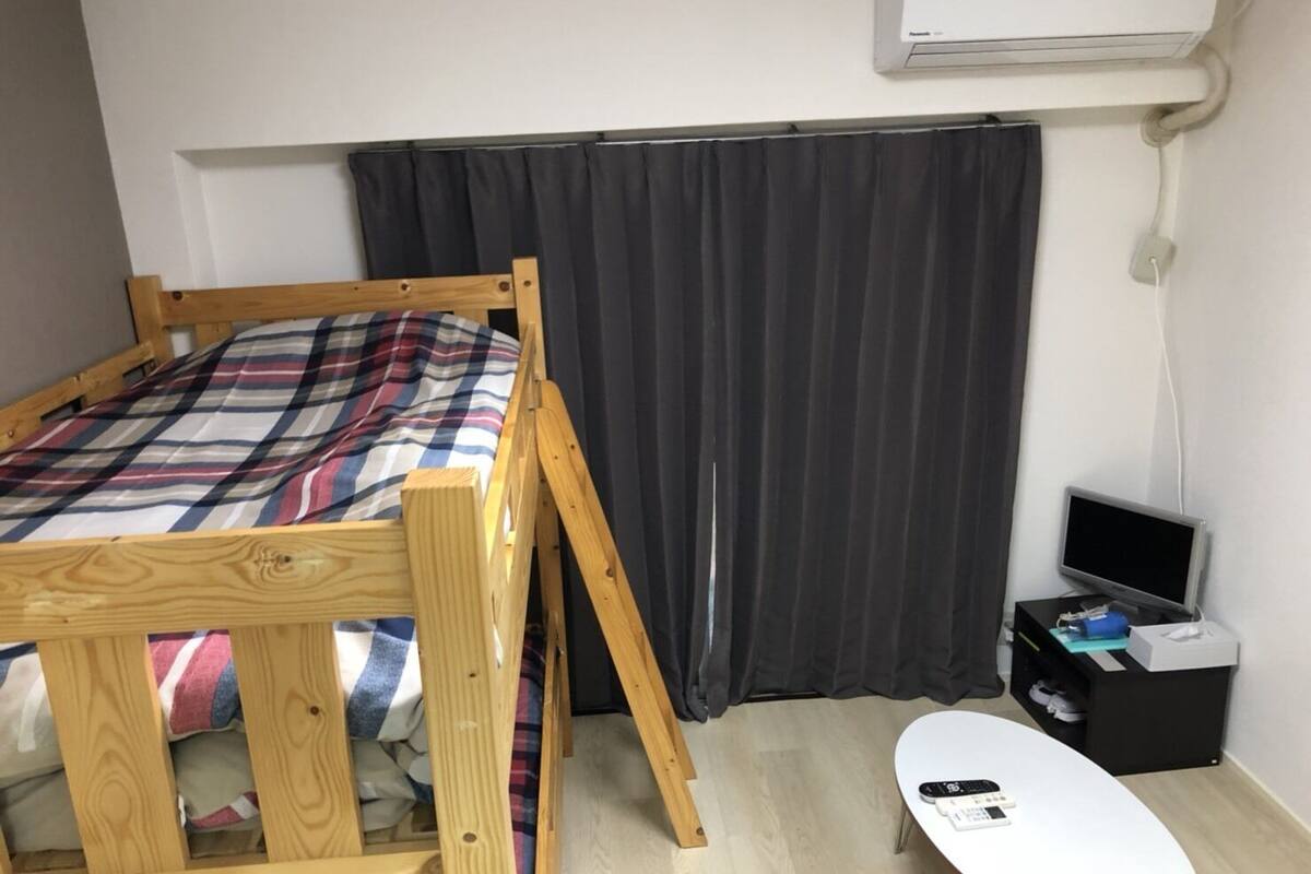 Une petite pièce avec un lit superposé en bois, un bureau avec un ordinateur et une table blanche.