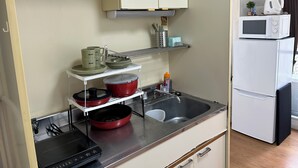 A compact kitchenette with a microwave, kettle, and a small shelf with kitchen utensils. - Guest House Zen Hakata Ohori Park 2 (Fukuoka)