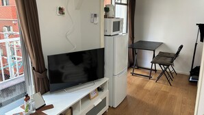 A compact living space with a flat-screen TV, a microwave, a small dining table, and a foldable chair. - Guest House Zen Hakata Ohori Park 2 (Fukuoka)