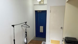 A hallway with a blue door, a coat rack, a vacuum cleaner, and a laptop on a table. - Guest House Zen Hakata Ohori Park 2 (Fukuoka)