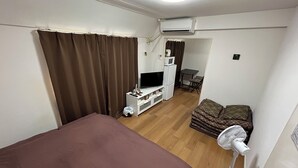 A hotel room with a bed, a TV, a mini-fridge, a microwave, a fan, and a small table with chairs. - Guest House Zen Hakata Ohori Park 2 (Fukuoka)