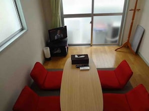 A room with a wooden table, red cushioned seating, a television, and a window with curtains.