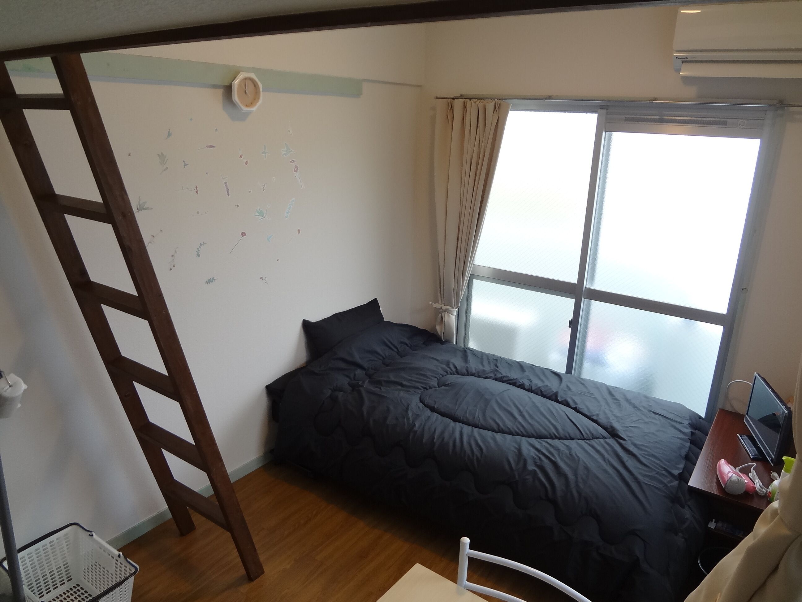 A bedroom with a bed, a window, a ladder, and a desk with a computer.