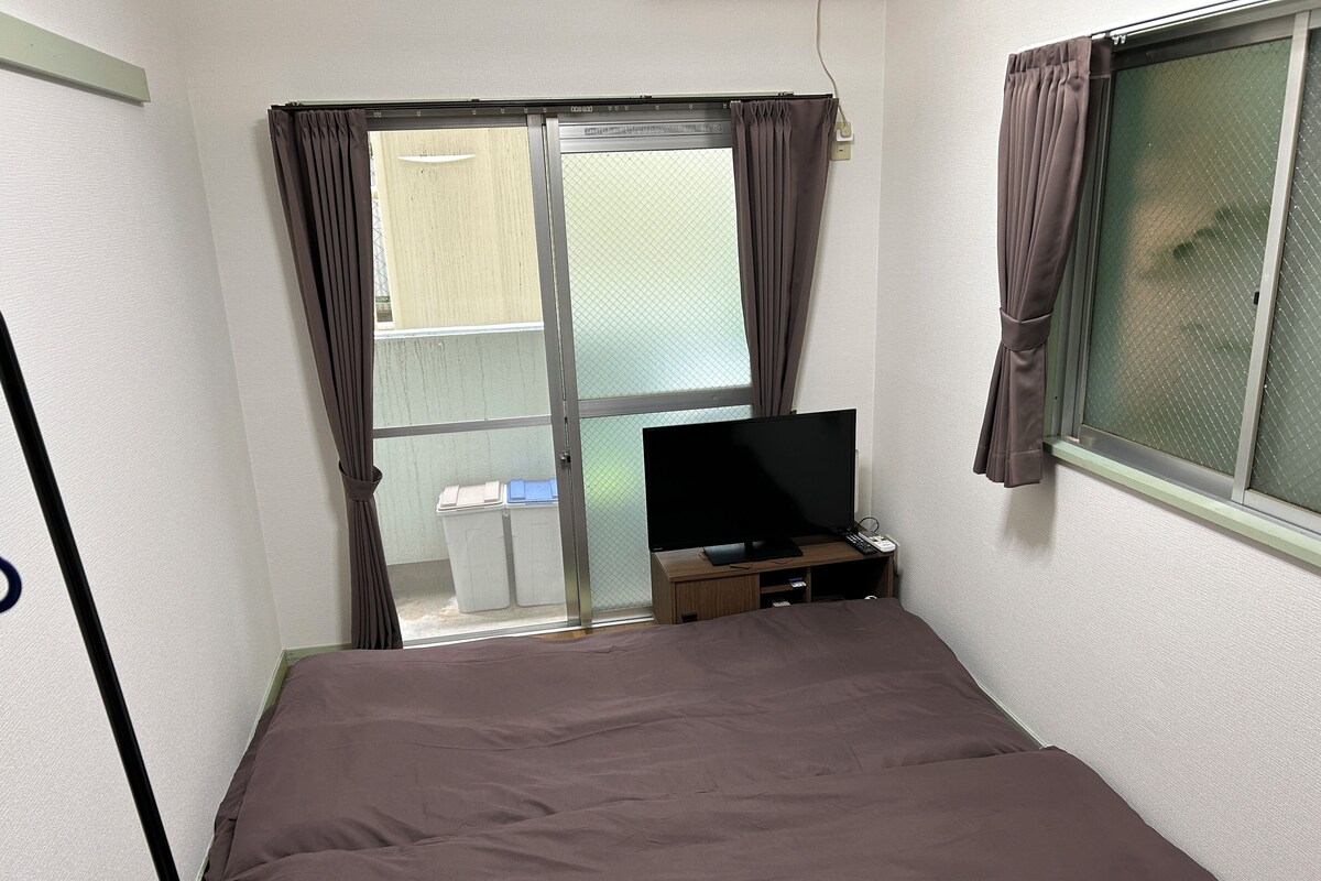 A bedroom with a bed, a TV, and a window with curtains.