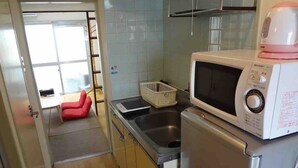 Een praktische keuken met een magnetron, spoelbak en een kleine koelkast. In de aangrenzende kamer staat een rode stoel.