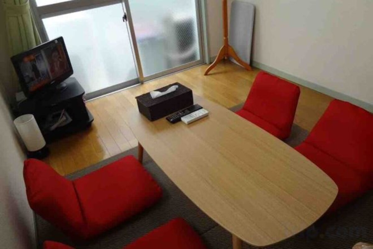 Une salle de conférence avec une table en bois, des chaises rouges, un téléviseur et un haut-parleur.