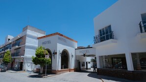A white building with "HOTEL" signage, arched entrances, and a balcony with a metal railing. - Hotel Zacatecas Courts (Zacatecas)