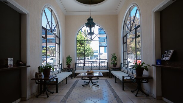 A spacious lobby with a high ceiling, large arched windows, and a central table with a bowl of fruit. - Hotel Zacatecas Courts (Zacatecas)