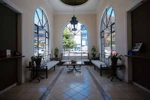 A spacious lobby with a high ceiling, large arched windows, and a central table with a bowl of fruit. - Hotel Zacatecas Courts (Zacatecas)