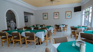 A dining area with tables covered in green tablecloths, wooden chairs, and a tiled floor. - Hotel Zacatecas Courts (Zacatecas)