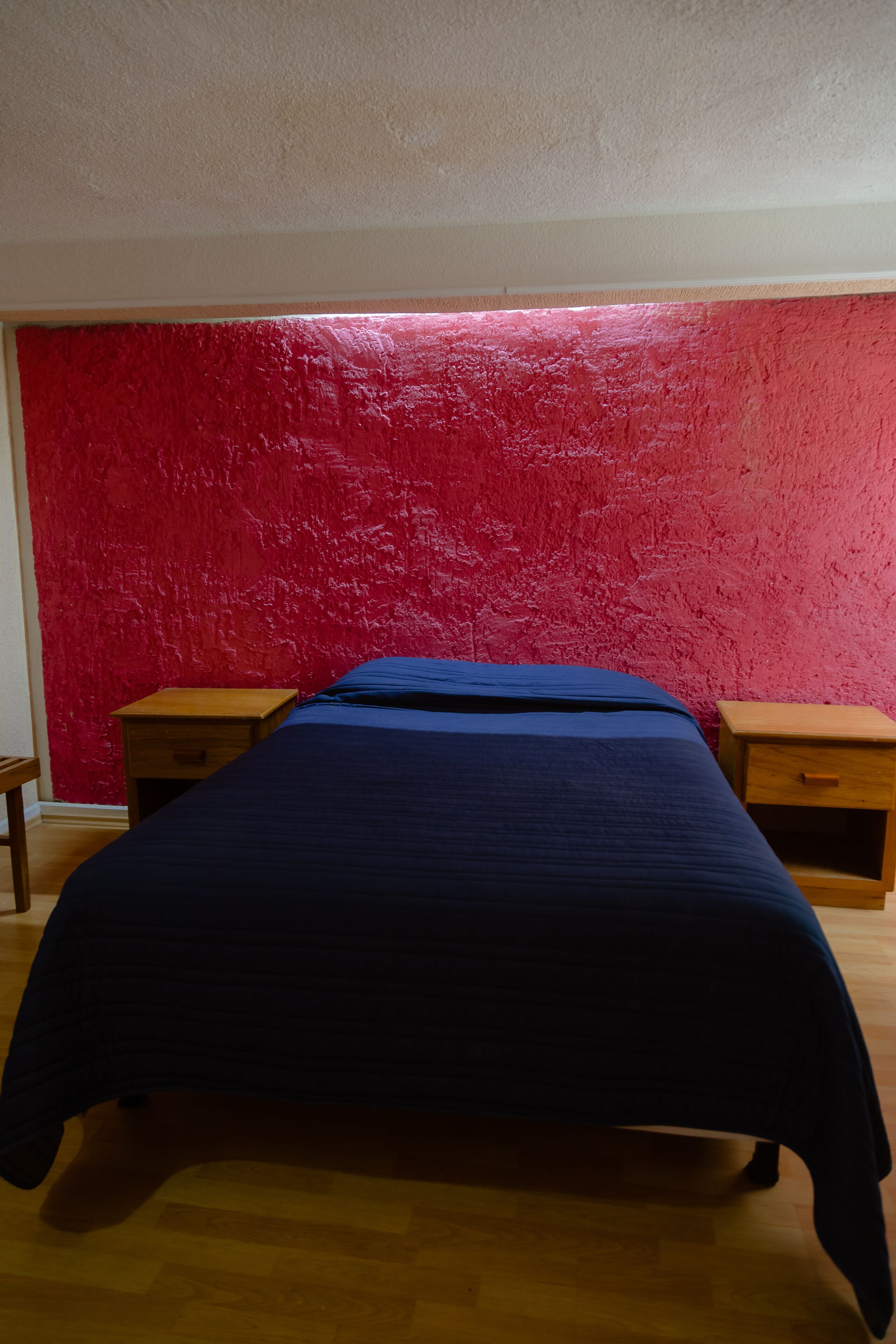 Una habitación con una cama, dos mesitas de noche de madera y una pared texturizada de color rojo.