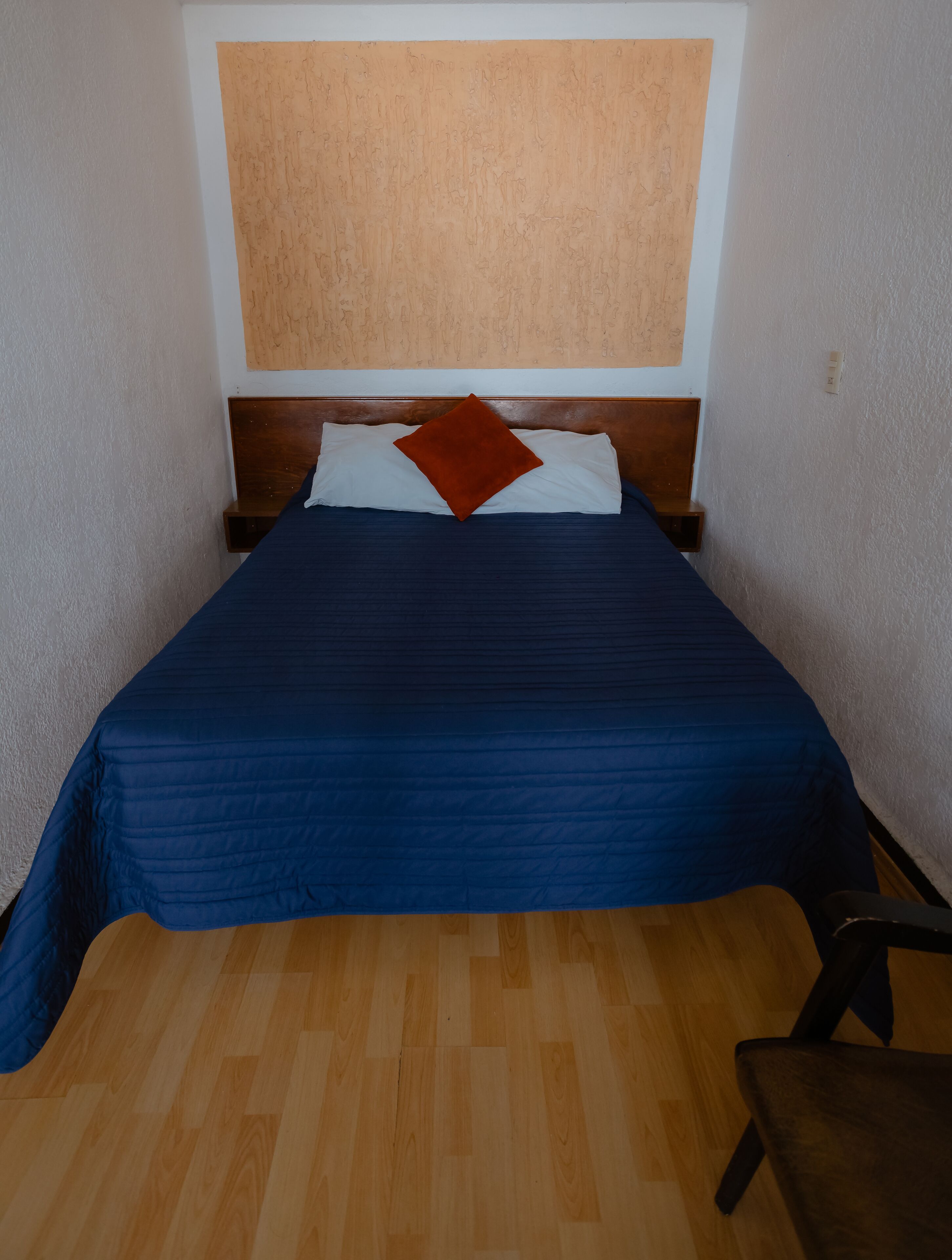 Een slaapkamer met een houten hoofdbord, een blauwe spreideken, een wit kussen en een bruin sierkussen.