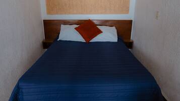 Een slaapkamer met een houten hoofdbord, een blauwe spreideken, een wit kussen en een bruin sierkussen.
