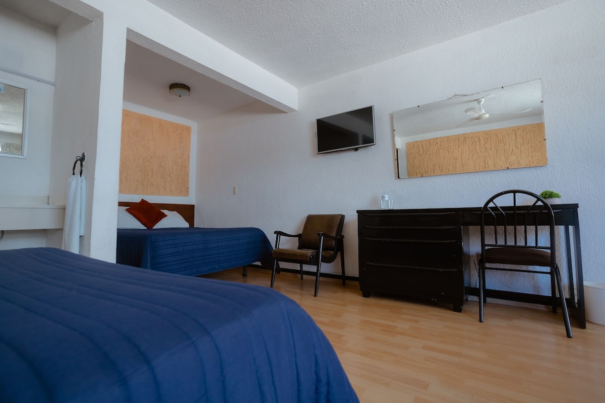 Ein Schlafzimmer mit Bett, Sessel, Schreibtisch, Fernseher und Spiegel.