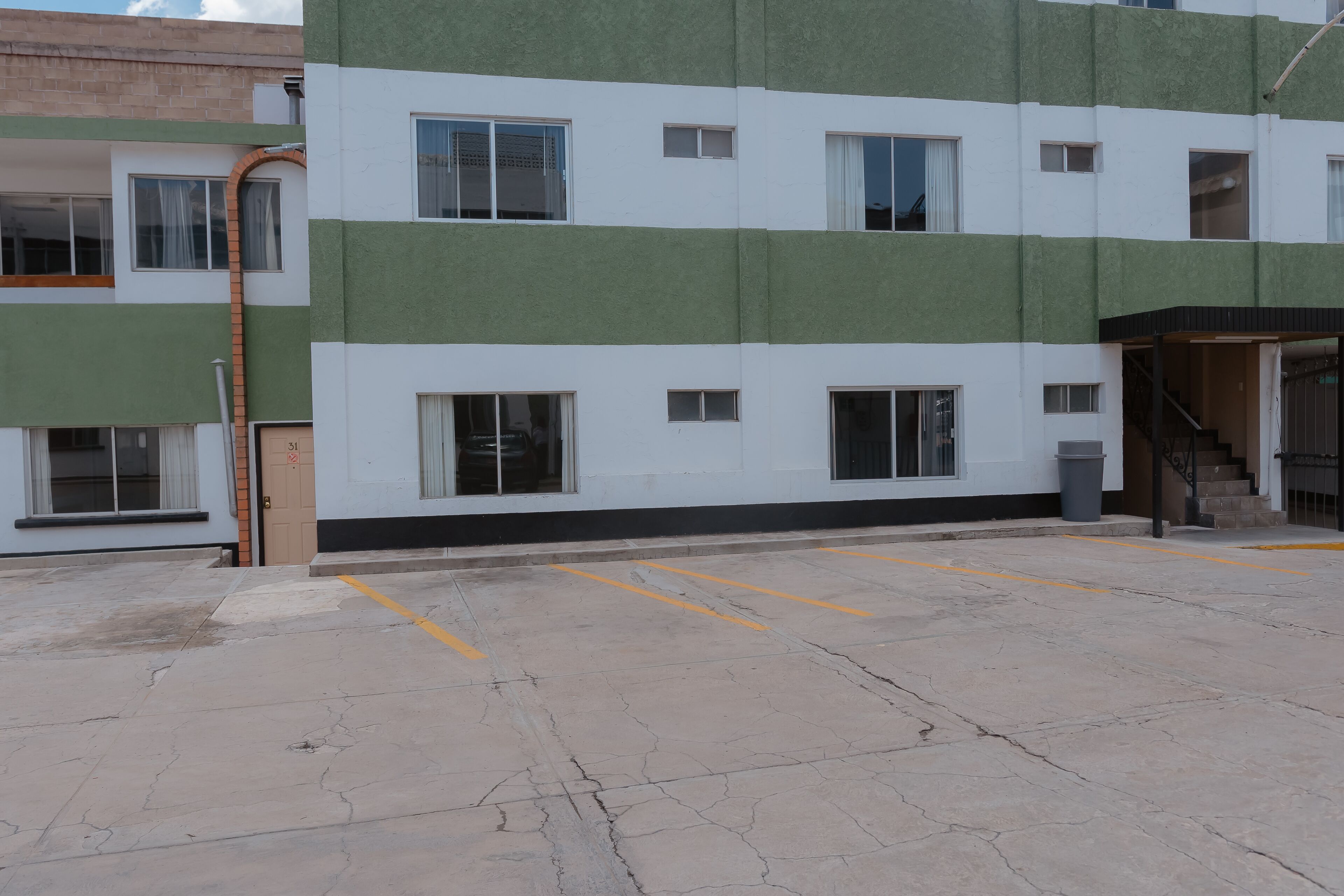 Un immeuble à plusieurs étages doté d’une façade sobre, de grandes fenêtres et d’un espace de stationnement délimité par des lignes jaunes.