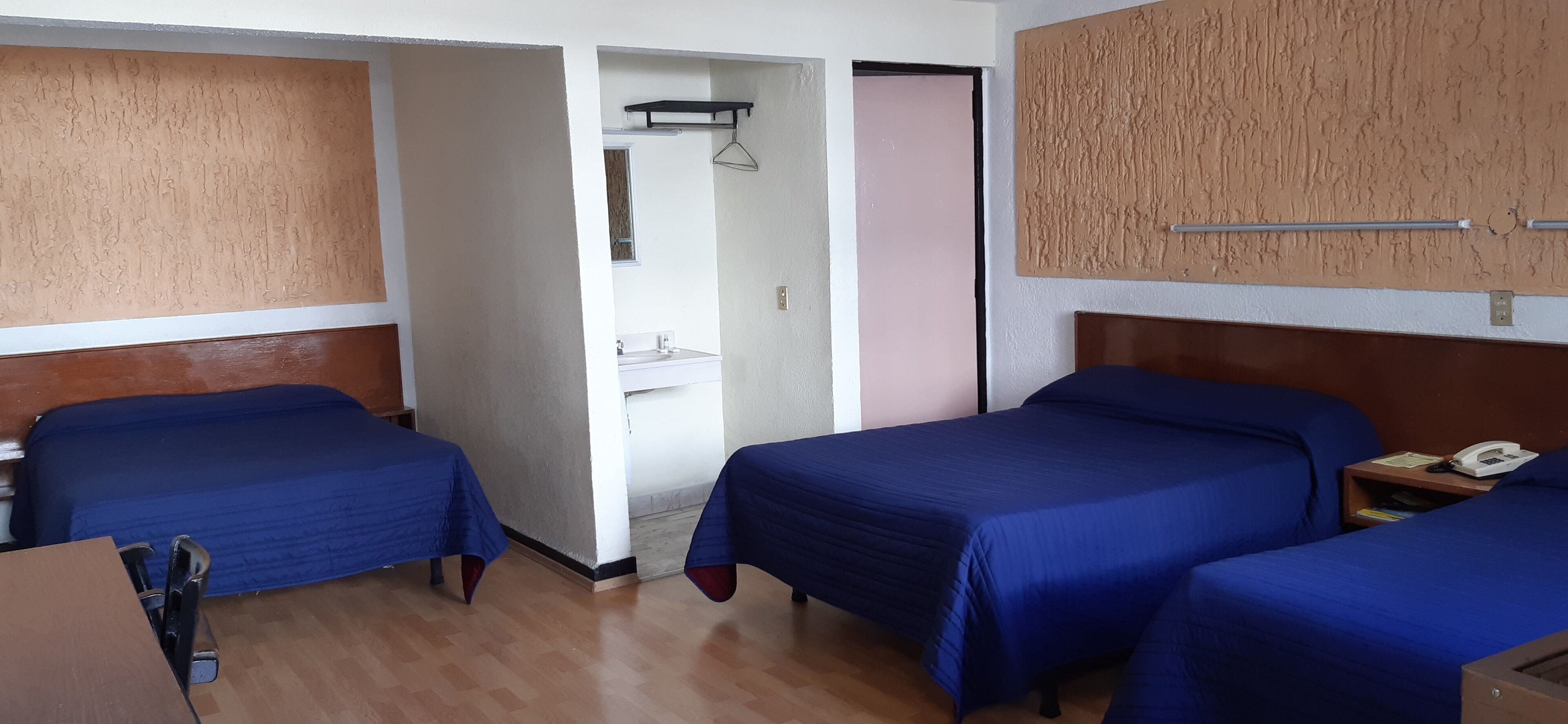 Habitación de hotel con dos camas, suelo de madera, pared blanca y puerta que da a un baño.