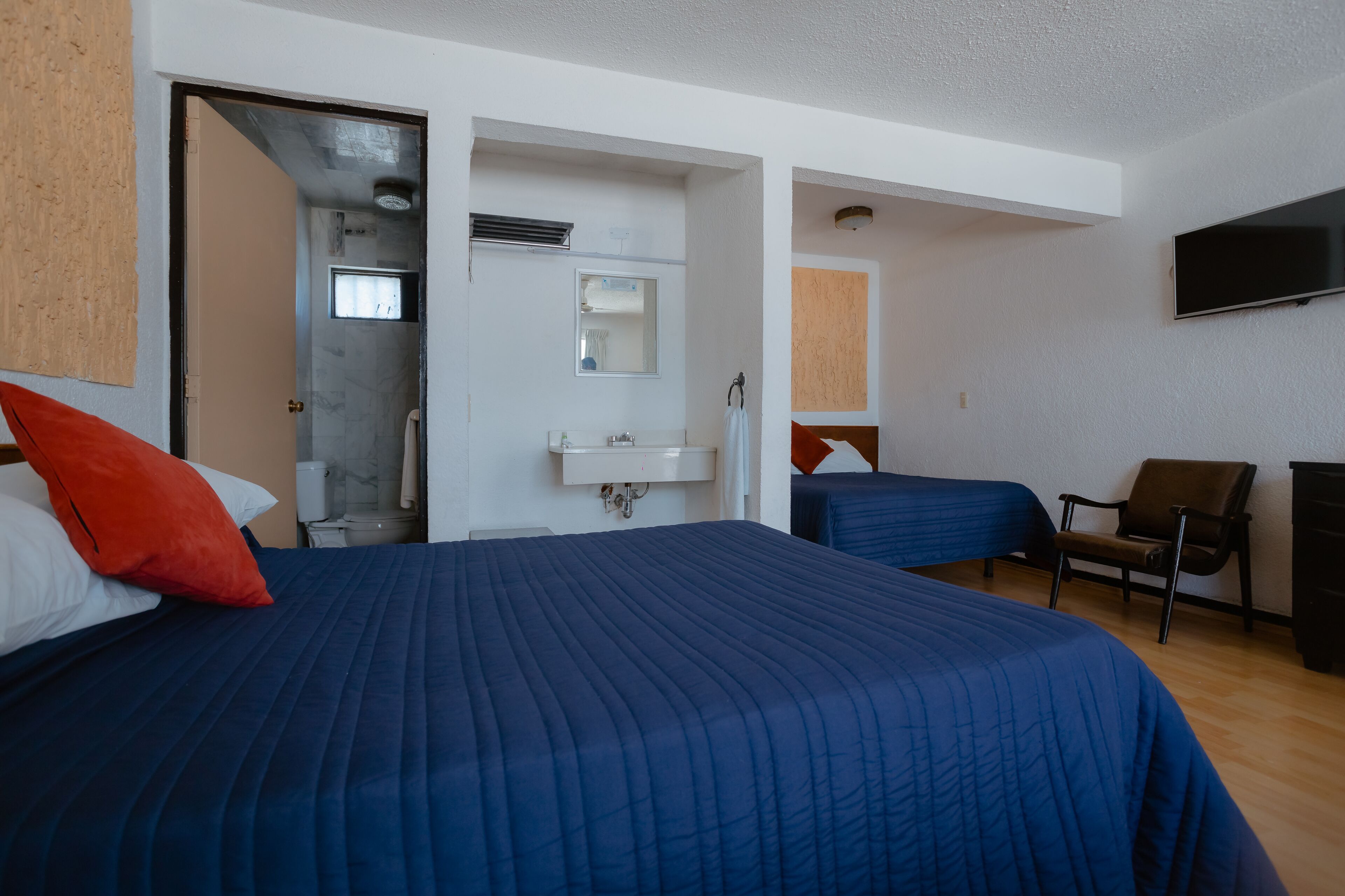 A hotel room with a large bed, a desk, a chair, a TV, and a bathroom with a shower and sink.