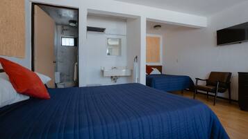 A hotel room with a large bed, a desk, a chair, a TV, and a bathroom with a shower and sink.
