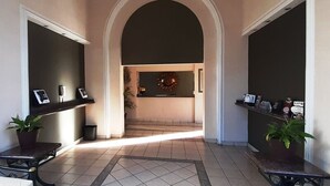 A hallway with a tiled floor, two potted plants, a reception desk, and a wall-mounted clock. - Hotel Zacatecas Courts (Zacatecas)