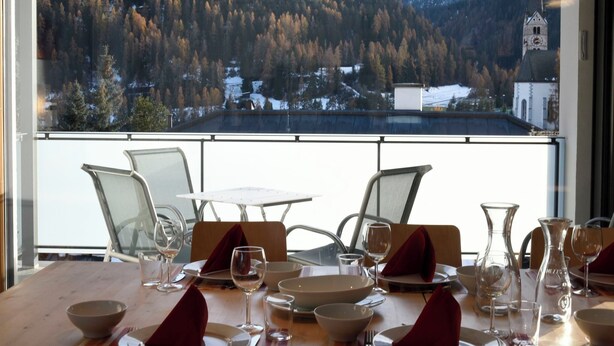Une table à manger dressée avec des assiettes, des verres et des couverts, donnant sur un paysage montagneux avec une église.