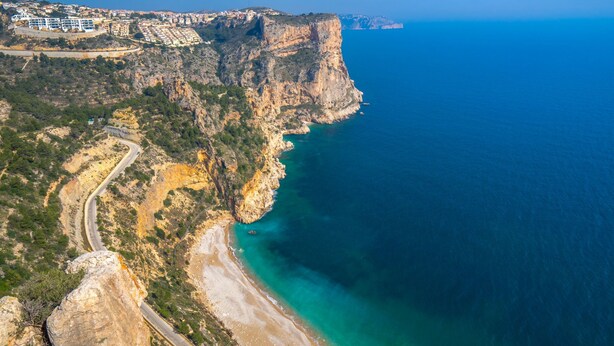 Un paisaje costero con una carretera sinuosa, una playa y un acantilado con vistas al mar.