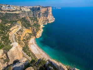 Paisagem costeira com uma estrada sinuosa, uma praia e um penhasco com vista para o mar.