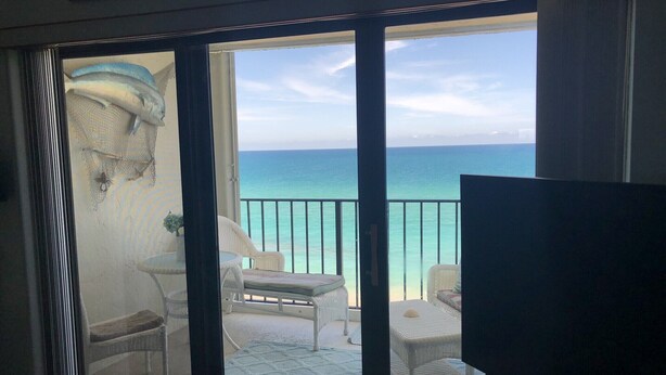 A balcony with a view of the sea, a television, and a dining area with chairs and a table. - Condo with 2 bedrooms (Jensen Beach)