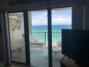 Un balcón con vista al mar, un televisor y un comedor con sillas y una mesa.