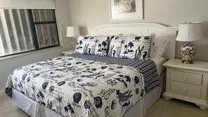 A bedroom with a bed, two bedside tables, a window with curtains, and a framed picture on the wall. - Condo with 2 bedrooms (Jensen Beach)