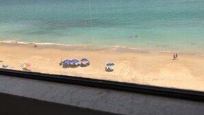A beach view with clear turquoise water, a sandy shore, and several umbrellas providing shade. - Condo with 2 bedrooms (Jensen Beach)