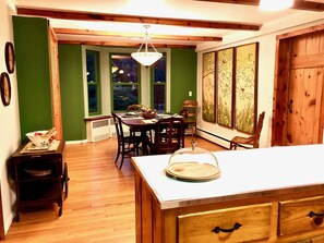 A dining area with a wooden table and chairs, a chandelier, and a view of greenery outside.