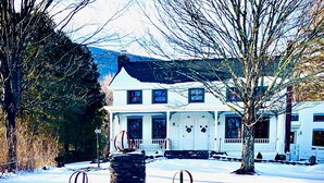 A white house with a stone fountain in the front yard, surrounded by snow.
