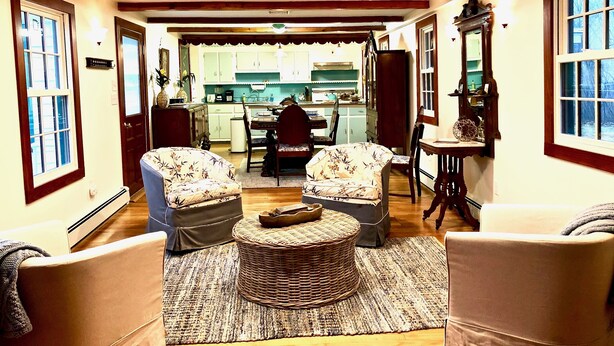 A cozy living room with two floral armchairs, a round wicker coffee table, and a dining area with a kitchen in the background.