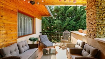 Un espace extérieur accueillant, aménagé avec des meubles en osier, un mur en pierre et offrant une vue sur les arbres.