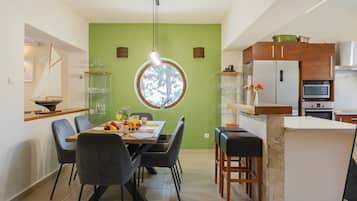 Une cuisine moderne avec un coin repas, dotée d’une fenêtre ronde, d’appareils électroménagers intégrés et d’un mur d’accent vert.