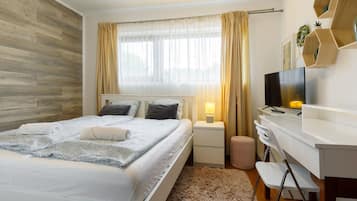 Une chambre à coucher moderne, avec un lit, des tables de chevet, un bureau, une chaise, un téléviseur et une fenêtre avec des rideaux.