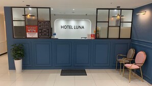 A reception desk with 'HOTEL LUNA' signage, a potted plant, and two chairs. - Hotel Luna (Hwaseong)