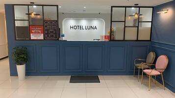 A reception desk with 'HOTEL LUNA' signage, a potted plant, and two chairs.