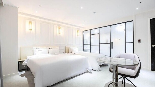 A modern hotel room with a large bed, a glass table, and a white chair. - Hotel Luna (Hwaseong)