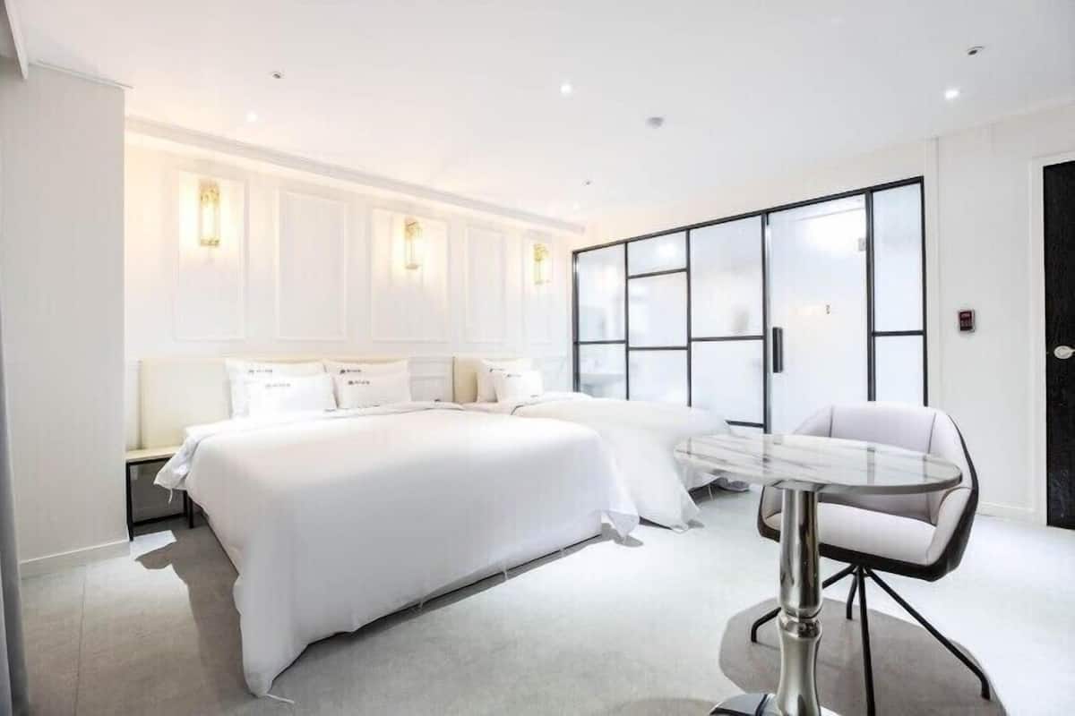 A modern hotel room with a large bed, a glass table, and a white chair.