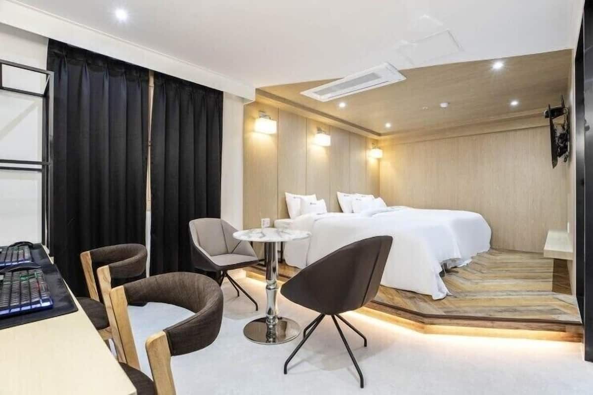 A hotel room with a bed, two chairs, a small table, and a desk with a keyboard.