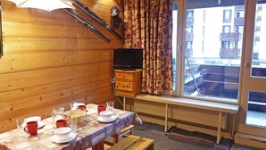 A wooden interior with a dining table set for four, a television, and a window with curtains.