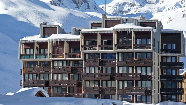 A multi-story hotel with balconies, set against a snowy mountain backdrop.