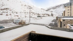 A snow-covered parking area with a wooden deck, a barbecue grill, and a building with a stone facade. - Beautiful apartment for 6 guests with WIFI and balcony (Les Boisses)