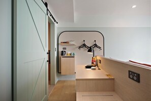 A modern hotel room with a wooden desk, a black lamp, and a small kitchenette area. - Sudima Auckland City (Auckland)