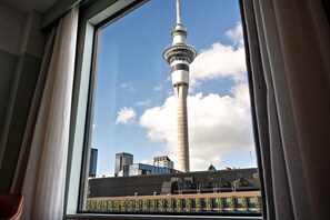 Uitzicht vanuit een raam op een hoge toren met een rond observatiedek, moderne gebouwen en een heldere lucht.
